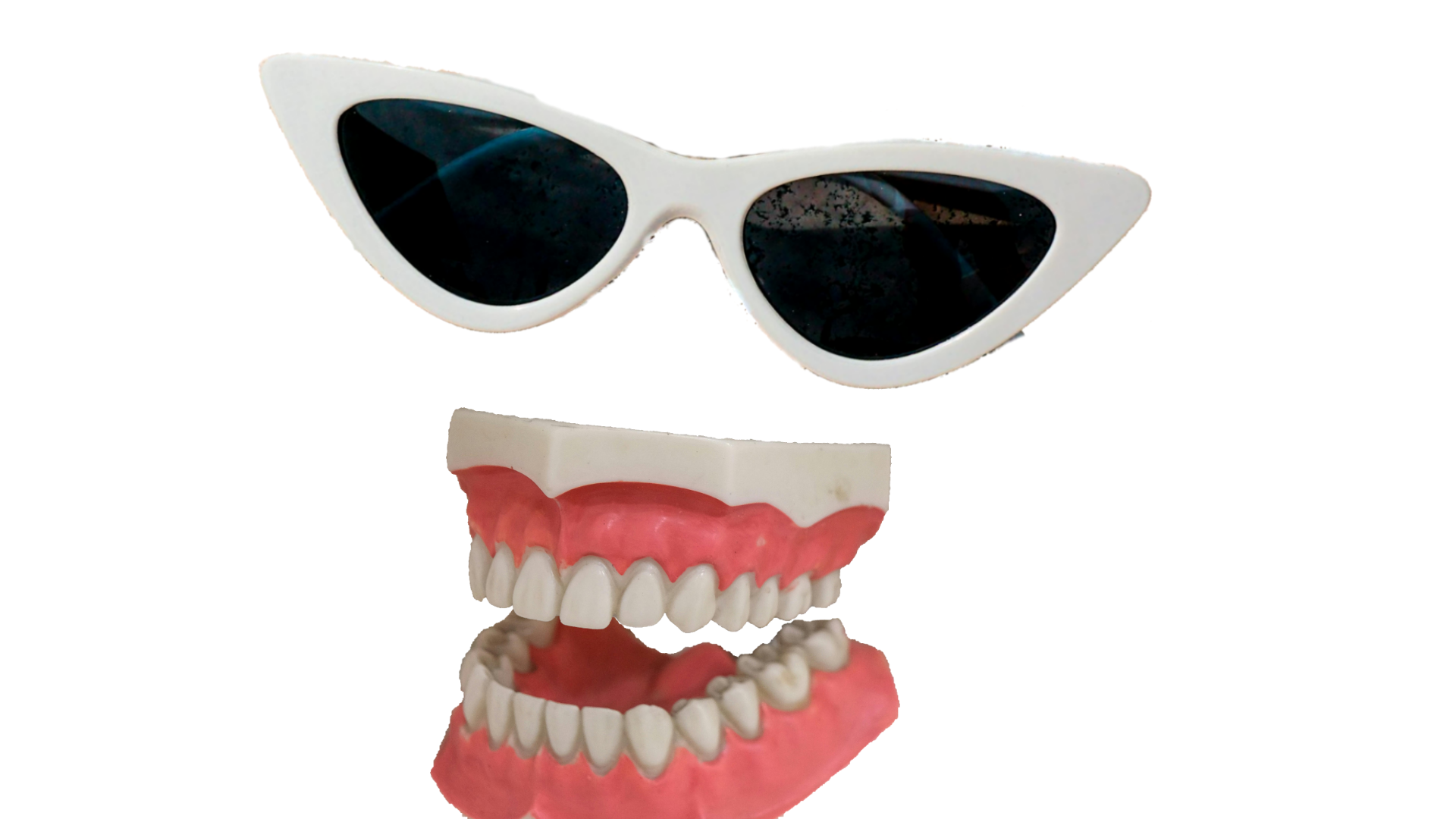 A picture of cat-eye sunglasses with white frames positioned over a set of false teeth.